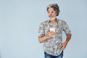 copo de bebida nas mãos. homem moderno elegante sênior com cabelos grisalhos e barba dentro de casa foto