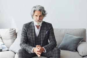 concepção de estilo bonito. homem moderno elegante sênior com cabelos grisalhos e barba dentro de casa foto