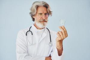 trabalhador médico detém lâmpada nas mãos. homem moderno elegante sênior com cabelos grisalhos e barba dentro de casa foto