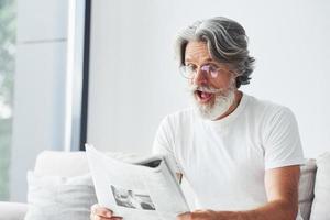 descansando no sofá. homem moderno elegante sênior com cabelos grisalhos e barba dentro de casa foto