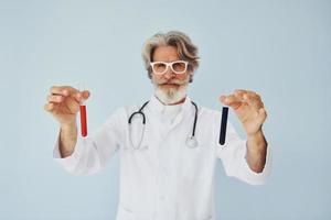 médico detém tubos de ensaio. homem moderno elegante sênior com cabelos grisalhos e barba dentro de casa foto