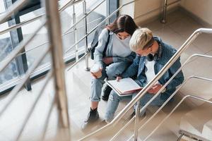 dois amigos jovens estudantes sentados e lendo um livro juntos nas escadas da faculdade foto