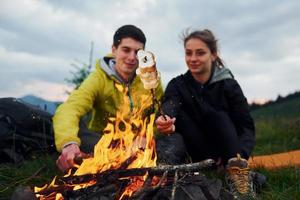 casal com marshmallow perto da fogueira. majestosas montanhas dos cárpatos. bela paisagem de natureza intocada foto