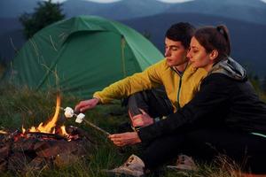 marshmallow clássico fazendo perto da fogueira. Jovem casal. majestosas montanhas dos cárpatos. bela paisagem de natureza intocada foto