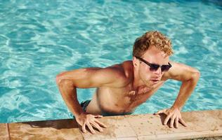 homem de óculos escuros está na piscina em suas férias foto