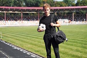 jogador de futebol no campo. jovem esportivo em camisa preta e calça ao ar livre durante o dia foto