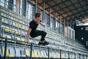 pulando e fazendo parkour nas arquibancadas. jovem esportivo em camisa preta e calça ao ar livre durante o dia foto