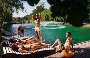 clima quente e ensolarado. grupo de jovens felizes se divertem na piscina durante o dia foto