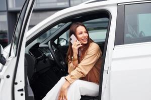 fala por telefone com a porta aberta. mulher jovem e bonita na moda e seu automóvel moderno foto