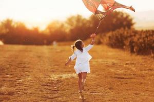 menina com roupas brancas correndo com pipa ao ar livre no campo foto