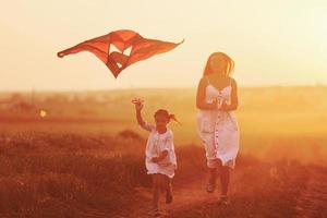 mãe feliz com sua filhinha se diverte brincando com pipa ao ar livre no campo foto