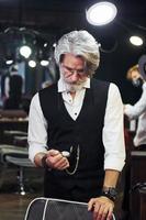 em roupas retrô na barbearia. elegante homem sênior moderno com cabelos grisalhos e barba está dentro de casa foto