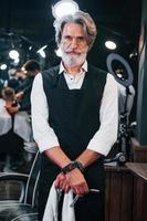 na barbearia. elegante homem sênior moderno com cabelos grisalhos e barba está dentro de casa foto