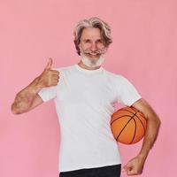 com bola de esporte nas mãos. elegante homem sênior moderno com cabelos grisalhos e barba está dentro de casa foto