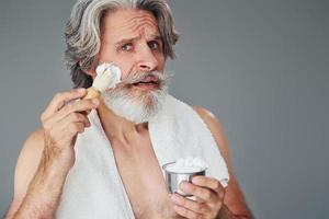 com gel de barbear. elegante homem sênior moderno com cabelos grisalhos e barba está dentro de casa foto