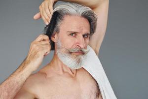 cuidando do corte de cabelo. elegante homem sênior moderno com cabelos grisalhos e barba está dentro de casa foto