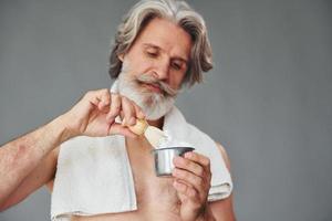 com gel de barbear. elegante homem sênior moderno com cabelos grisalhos e barba está dentro de casa foto