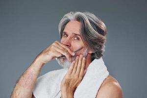 cuidando da barba. elegante homem sênior moderno com cabelos grisalhos está dentro de casa foto