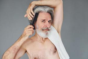 cuidando do corte de cabelo. elegante homem sênior moderno com cabelos grisalhos e barba está dentro de casa foto