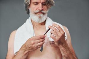 cuidando da barba. elegante homem sênior moderno com cabelos grisalhos está dentro de casa foto