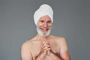 com toalha branca na cabeça. elegante homem sênior moderno com cabelos grisalhos e barba está dentro de casa foto