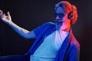 curtindo música. iluminação neon. elegante homem sênior moderno com cabelos grisalhos e barba está dentro de casa foto