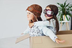 sentado na caixa de papel. duas meninas bonitinhas dentro de casa juntas. com óculos de piloto retrô e chapéu foto