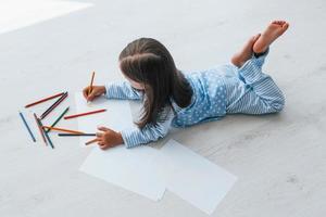 deitada no chão e desenhando. menina bonitinha dentro de casa sozinha foto