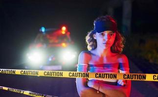 linda garota jovem com cabelo encaracolado e chapéu em pé ao ar livre perto da fita de linha da polícia. concepção de crime ou motim foto