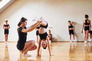 treinador está ajudando. grupo de crianças do sexo feminino praticando exercícios atléticos juntos dentro de casa foto