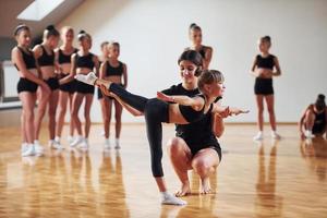 mulher ensinando e ajudando. grupo de crianças do sexo feminino praticando exercícios atléticos juntos dentro de casa foto