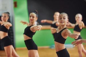 em pé e fazendo movimentos sincronizados. grupo de crianças do sexo feminino praticando exercícios atléticos juntos dentro de casa foto