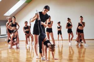 com ajuda do treinador. grupo de crianças do sexo feminino praticando exercícios atléticos juntos dentro de casa foto