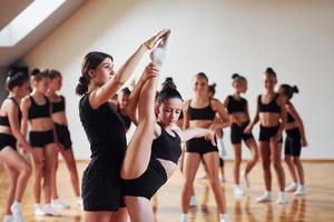 com ajuda do treinador. grupo de crianças do sexo feminino praticando exercícios atléticos juntos dentro de casa foto