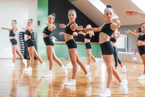 em pé e fazendo movimentos sincronizados. grupo de crianças do sexo feminino praticando exercícios atléticos juntos dentro de casa foto