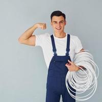 segura o cabo. trabalhador do sexo masculino em pé uniforme azul dentro do estúdio contra fundo branco foto