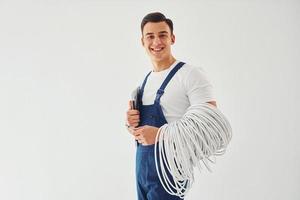 contém cabos, bloco de notas e chave de fenda. trabalhador do sexo masculino em pé uniforme azul dentro do estúdio contra fundo branco foto