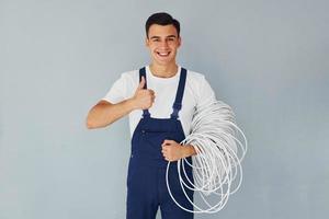 segura o cabo. trabalhador do sexo masculino em pé uniforme azul dentro do estúdio contra fundo branco foto