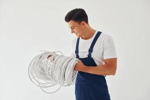 segura o cabo. trabalhador do sexo masculino em pé uniforme azul dentro do estúdio contra fundo branco foto