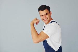 mostra o bíceps. Pronto para trabalhar. trabalhador masculino em pé uniforme azul dentro do estúdio contra fundo branco foto