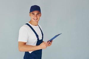 na tampa e com bloco de notas. trabalhador do sexo masculino em pé uniforme azul dentro do estúdio contra fundo branco foto