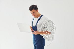 usa notebook. trabalhador do sexo masculino em pé uniforme azul dentro do estúdio contra fundo branco foto