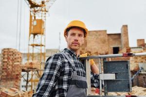 escada nas mãos. trabalhador da construção civil em equipamentos uniformes e de segurança tem trabalho na construção foto