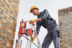 usa broca de mistura. trabalhador da construção civil em equipamentos uniformes e de segurança tem trabalho na construção foto