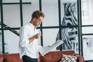 lê jornal. cara jovem caucasiano elegante camisa branca dentro de casa foto