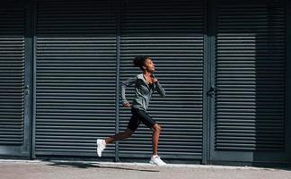 vista lateral da jovem afro-americana em roupas esportivas que corre perto da parede foto