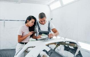 jovem mulher com homem trabalha juntos na garagem de reparação de automóveis foto