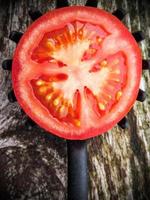 meio tomate em uma colher dentada de cozinha em uma velha mesa de madeira. imagem vertical. foto