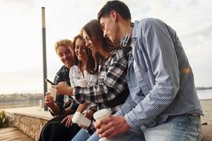 tempo ensolarado. bebendo café. grupo de jovens amigos alegres que está ao ar livre se divertindo juntos foto