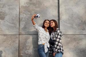 fazendo selfie. lindas amigas alegres ou casal de lésbicas juntos perto da parede ao ar livre durante o dia foto